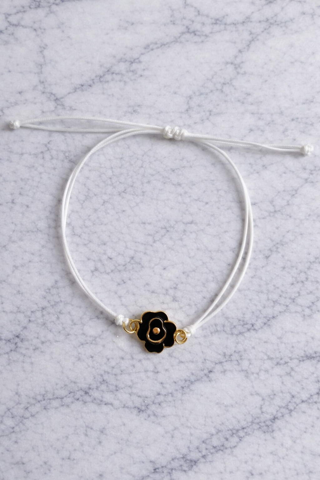 le bracelet a une fleur en métal de couleur or et noir le cordon et blanc 