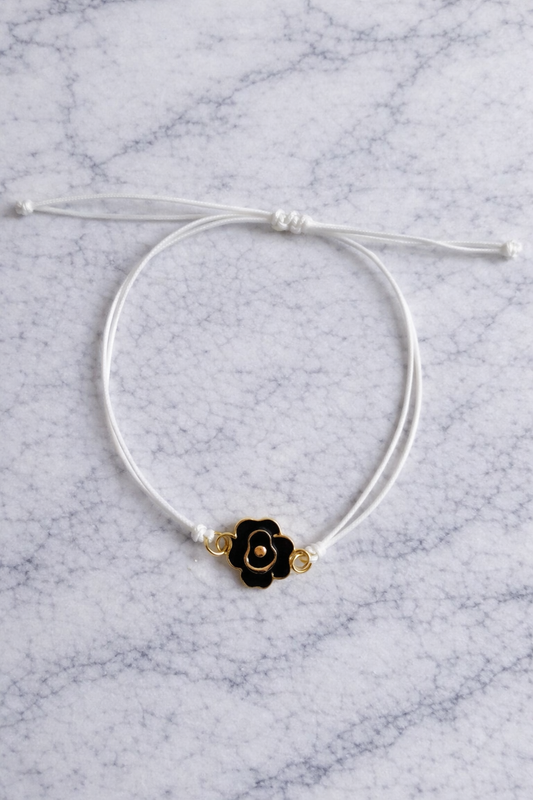 le bracelet a une fleur en métal de couleur or et noir le cordon et blanc 